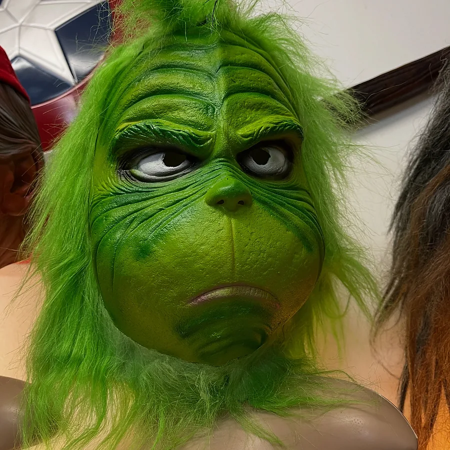 Furry green Christmas creature mask with a grumpy grin on a display bust