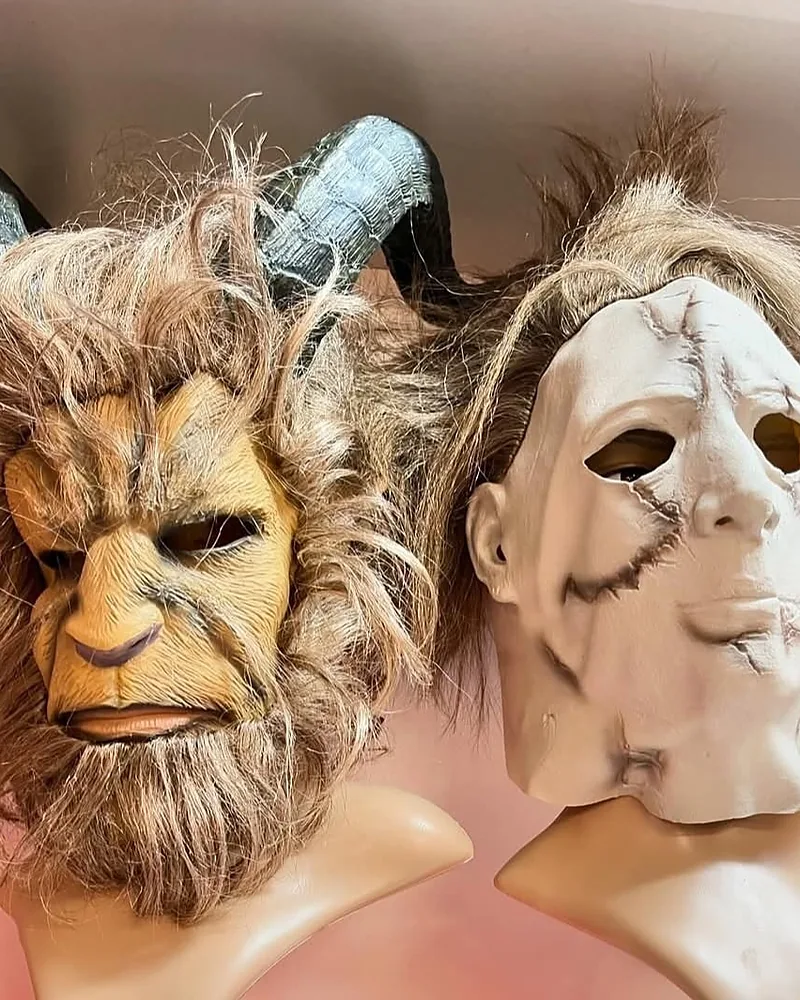 Two masks on display busts: a horned beast with a shaggy mane and a pale, scarred slasher mask