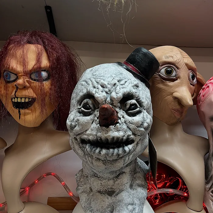 Shelf of horror masks on display busts, including a killer doll and a creepy snowman