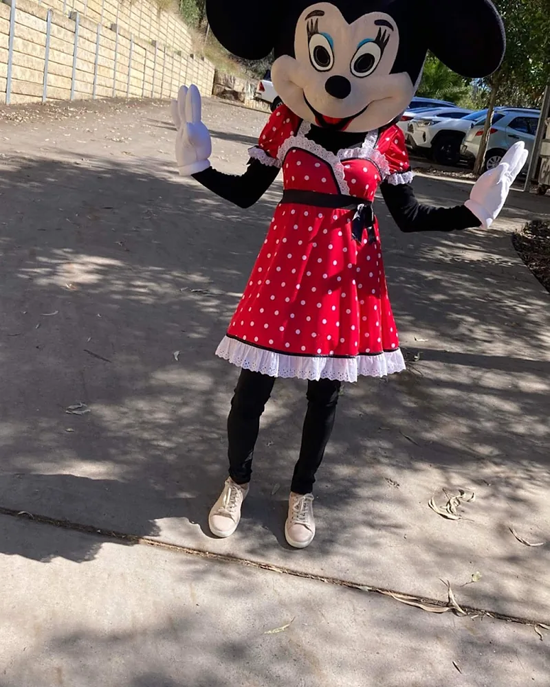 Full mascot costume of a cartoon mouse in a red polka dot dress, waving outdoors