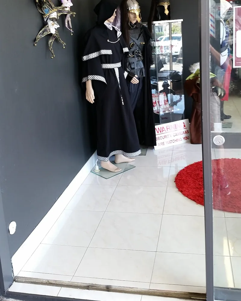 Mannequins in long dark robes and armour inside the shop entrance, with a jester mask on the wall