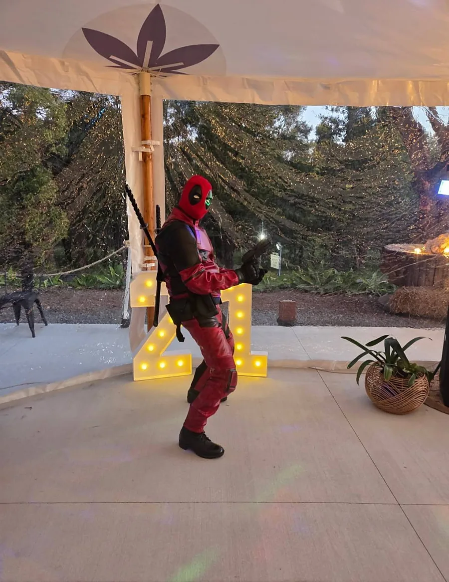 Masked red and black full-suit character dancing at a 21st birthday party under marquee letters