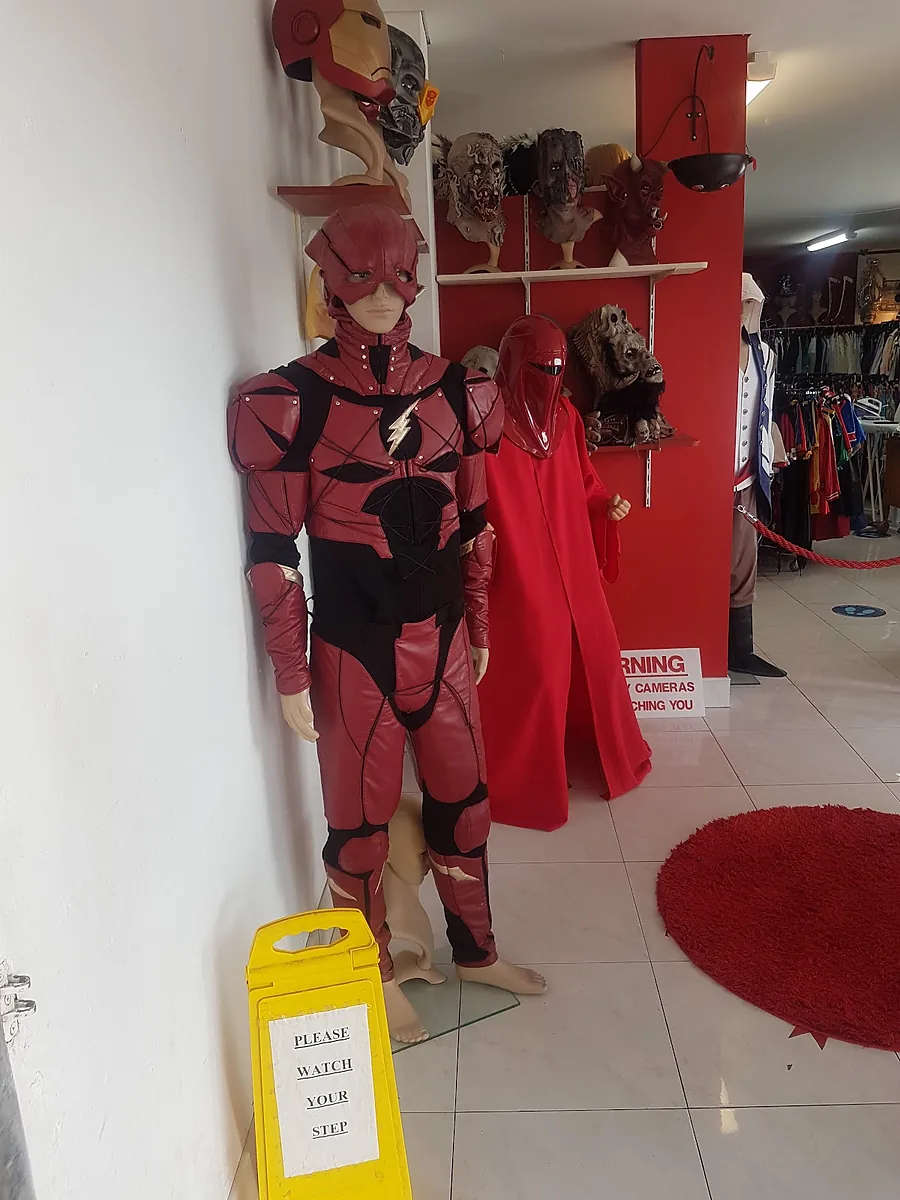 Showroom entry with a red superhero suit, a red robe, masks on shelves and racks beyond