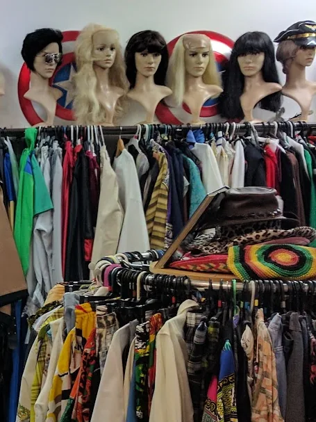 Row of wigs on display heads above a rack of colourful costumes
